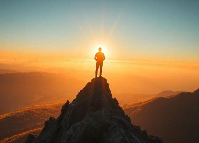 A person standing on a mountain peak, surrounded by a brilliant light